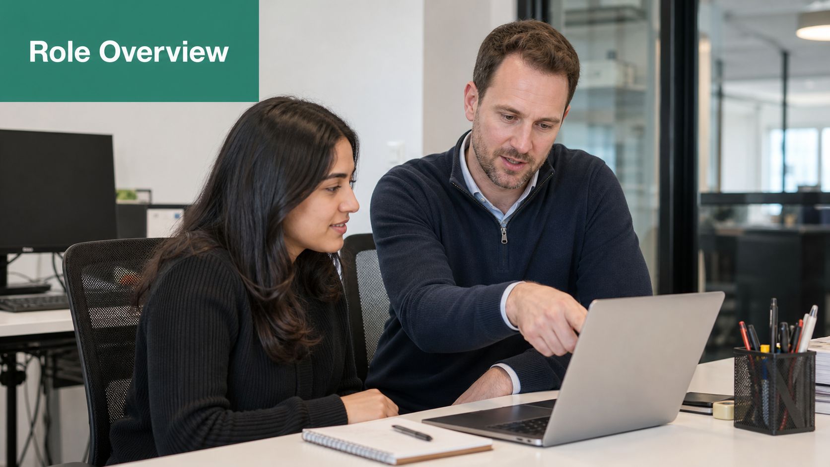 A professional man and woman working together at a laptop in a modern office environment.
